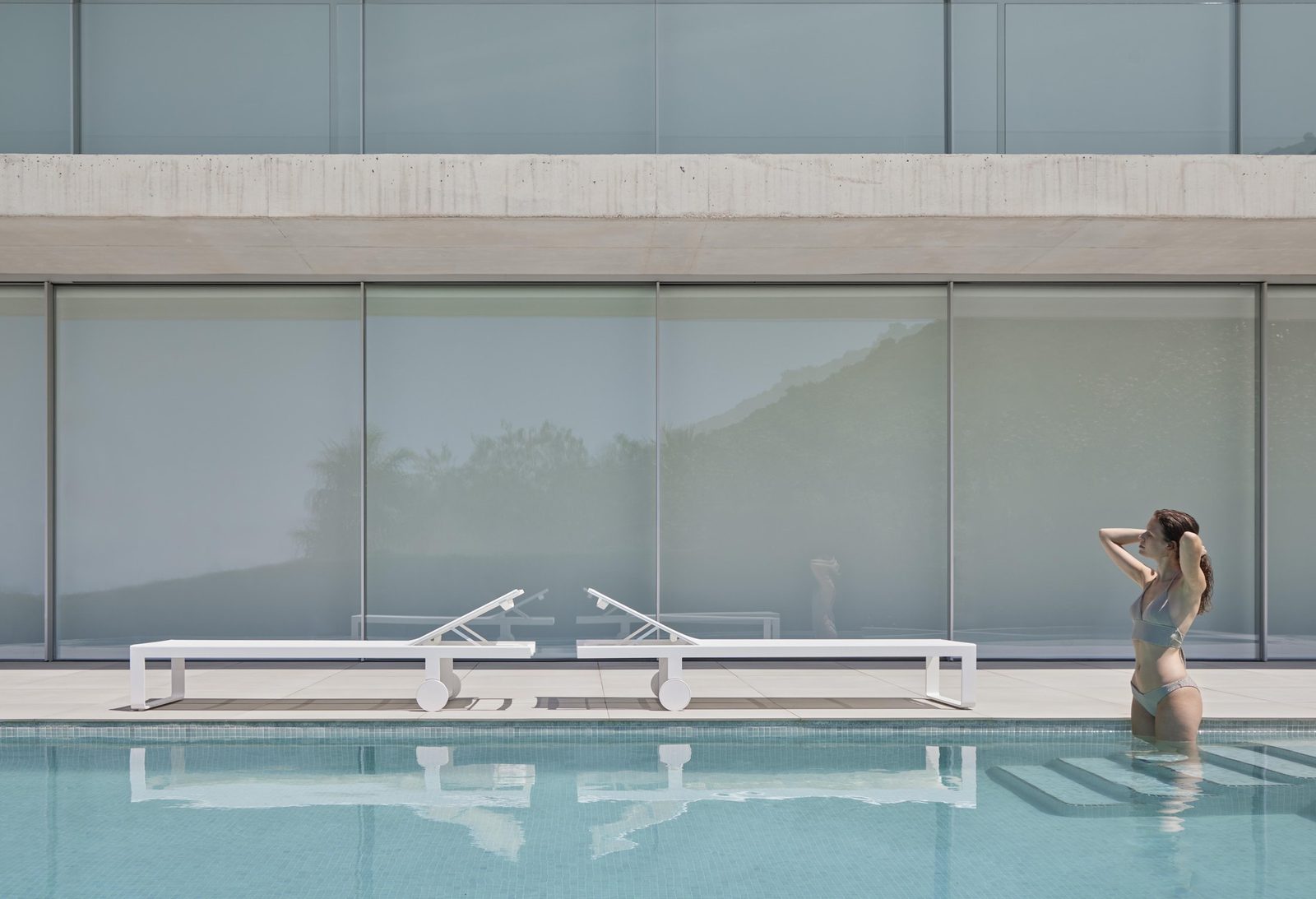 Flat Textil high chaise lounges at a glass-walled pool.